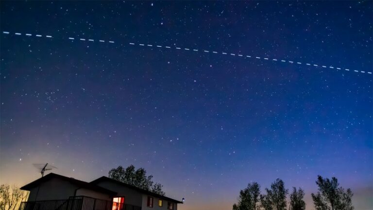 A line of bright spots representing satellites are seen in the night sky above a home